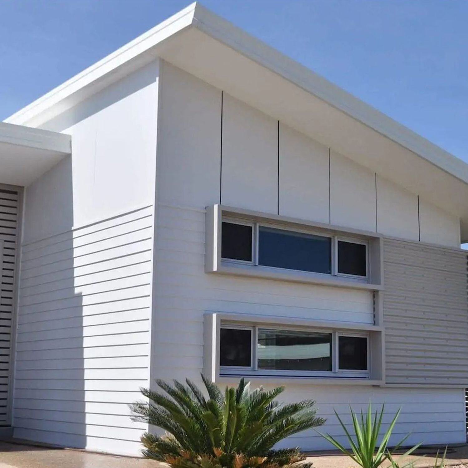 Fachada moderna y elegante de dos pisos con revestimiento Eterboard (fibrocemento) Innova Cladding color blanco, destacando dilataciones en día soleado.